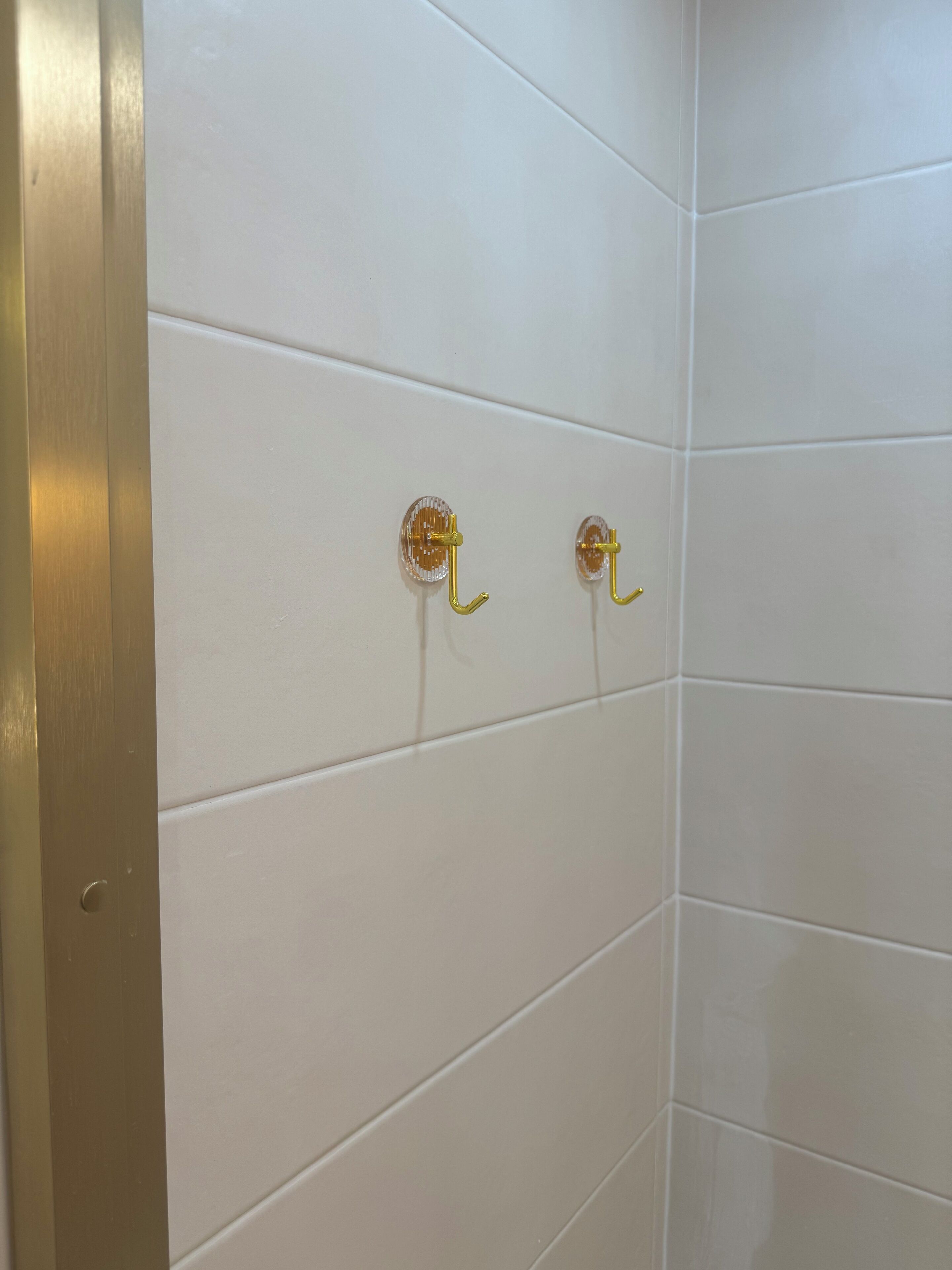 Un coin de pièce aux murs recouverts de carreaux blancs et dont le cadre de porte est de couleur dorée.