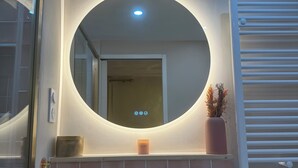 Ein Badezimmer mit rundem Spiegel, Waschbecken in Weiß und einem Handtuchhalter.