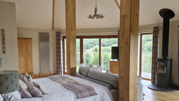 A spacious bedroom with a large bed, wooden beams, a fireplace, and a view of the outdoors.