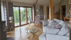 A spacious living room with a high ceiling, a glass coffee table, a grey sofa, and a dining area with chairs and a table.