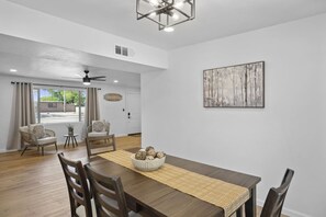 Un coin repas avec une table en bois, des chaises, un récipient contenant des objets décoratifs et un tableau accroché au mur.