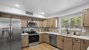 A modern kitchen with stainless steel appliances, wooden cabinets, and a large window providing natural light. - Boho on Bermuda with Private Pool in Tucson (Tucson)