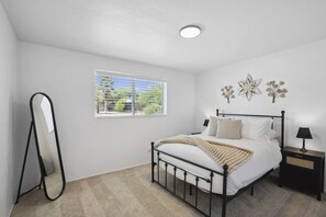 Un dormitorio con cama, mesita de noche, espejo y ventana con vistas a zonas verdes.