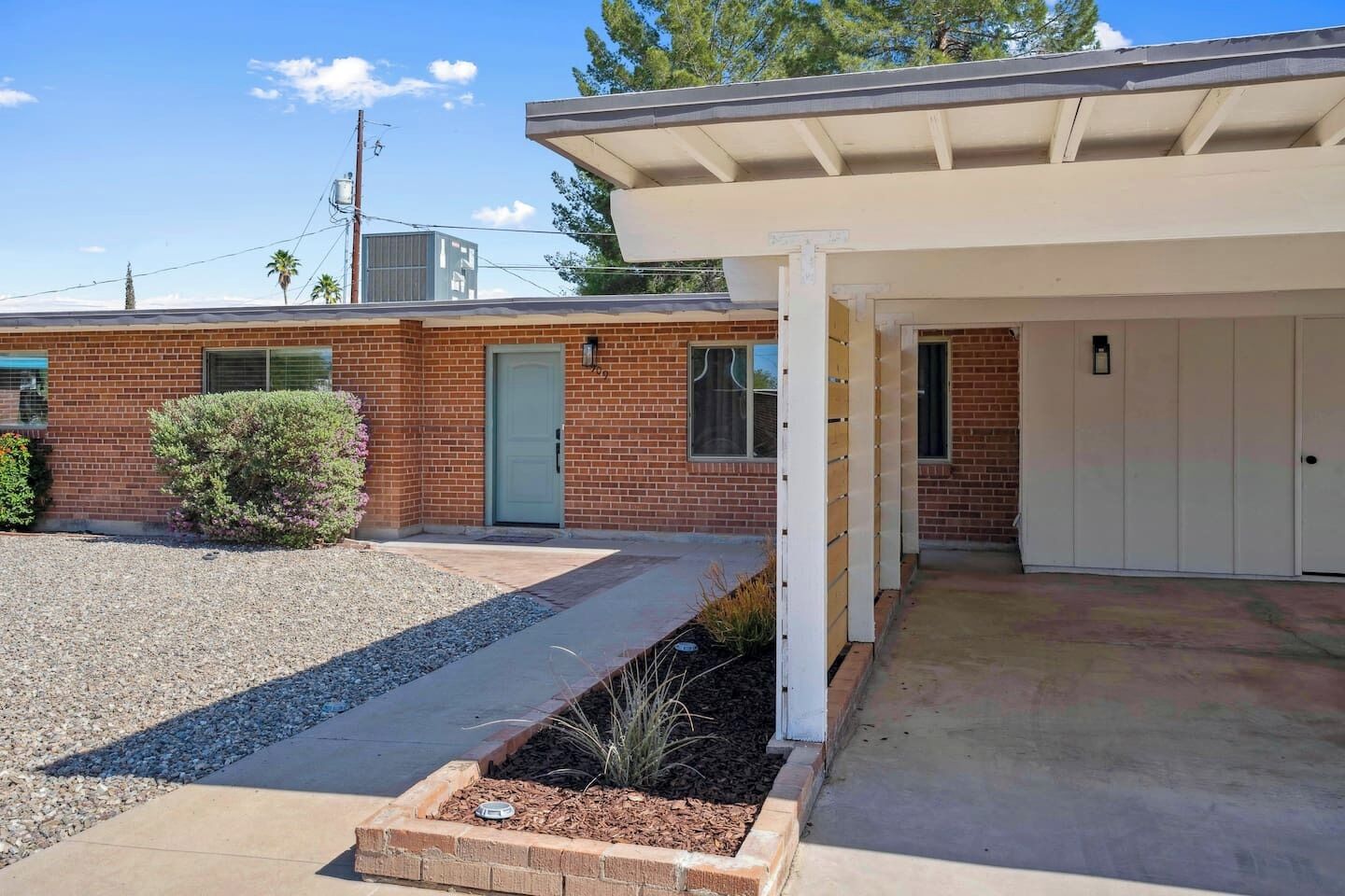 A residential building with a brick facade, a covered porch, and a gravel driveway.