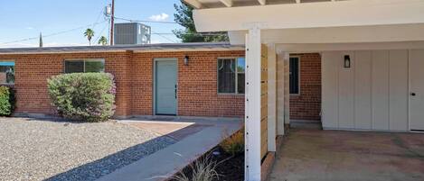 A residential building with a brick facade, a covered porch, and a gravel driveway.