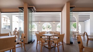 Un vaste espace intérieur aménagé en salle à manger, avec des tables et des chaises en bois, de grandes fenêtres et une vue sur l’extérieur.