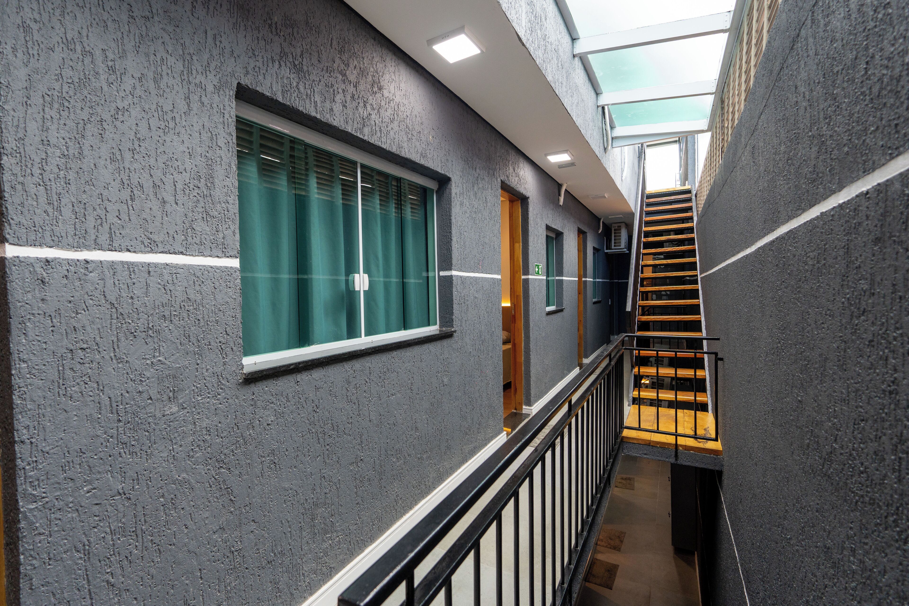 A modern hallway with grey textured walls, a black railing, and a wooden staircase with yellow steps.