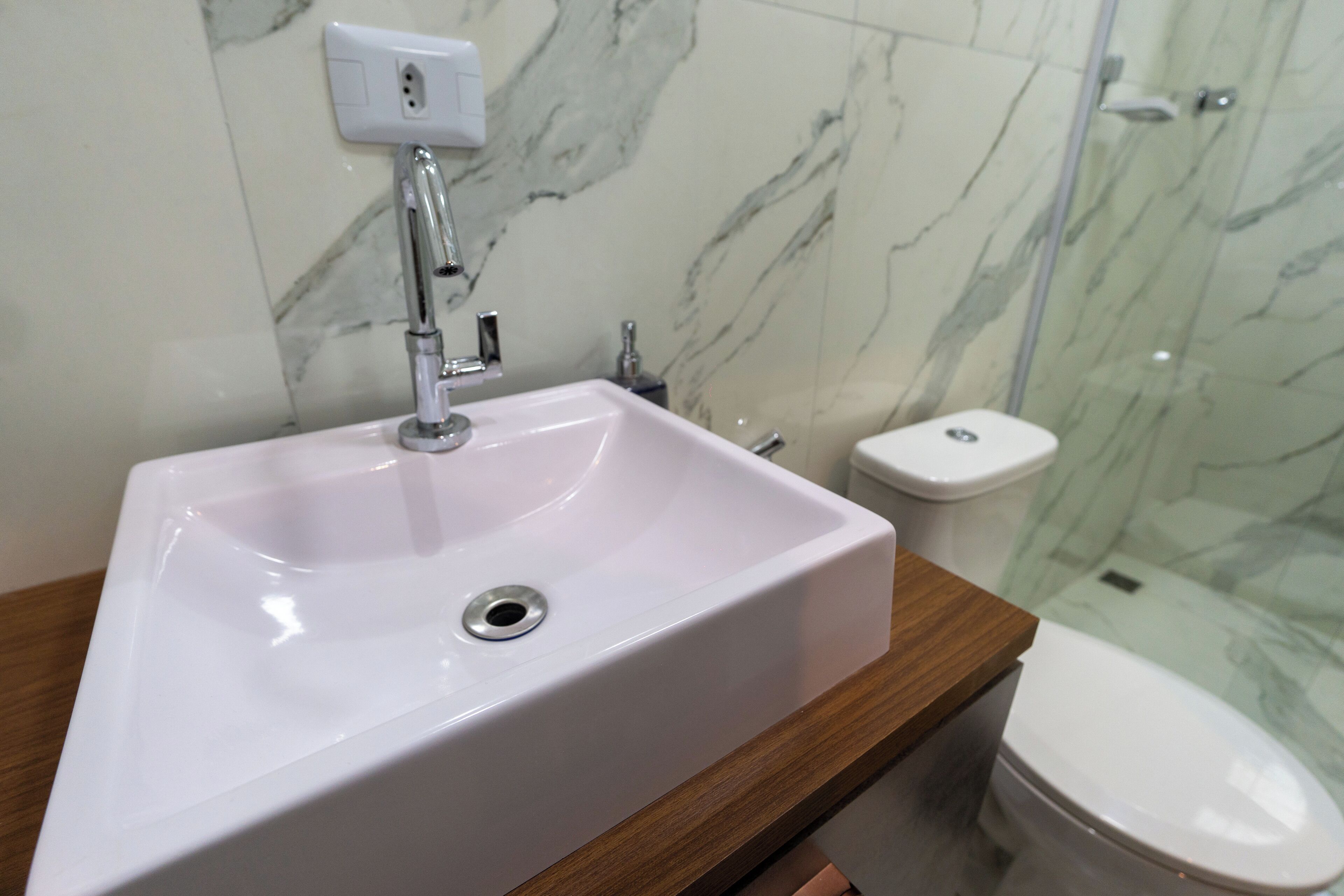 A bathroom with a white sink, a wooden countertop, a white toilet, and a glass shower enclosure.