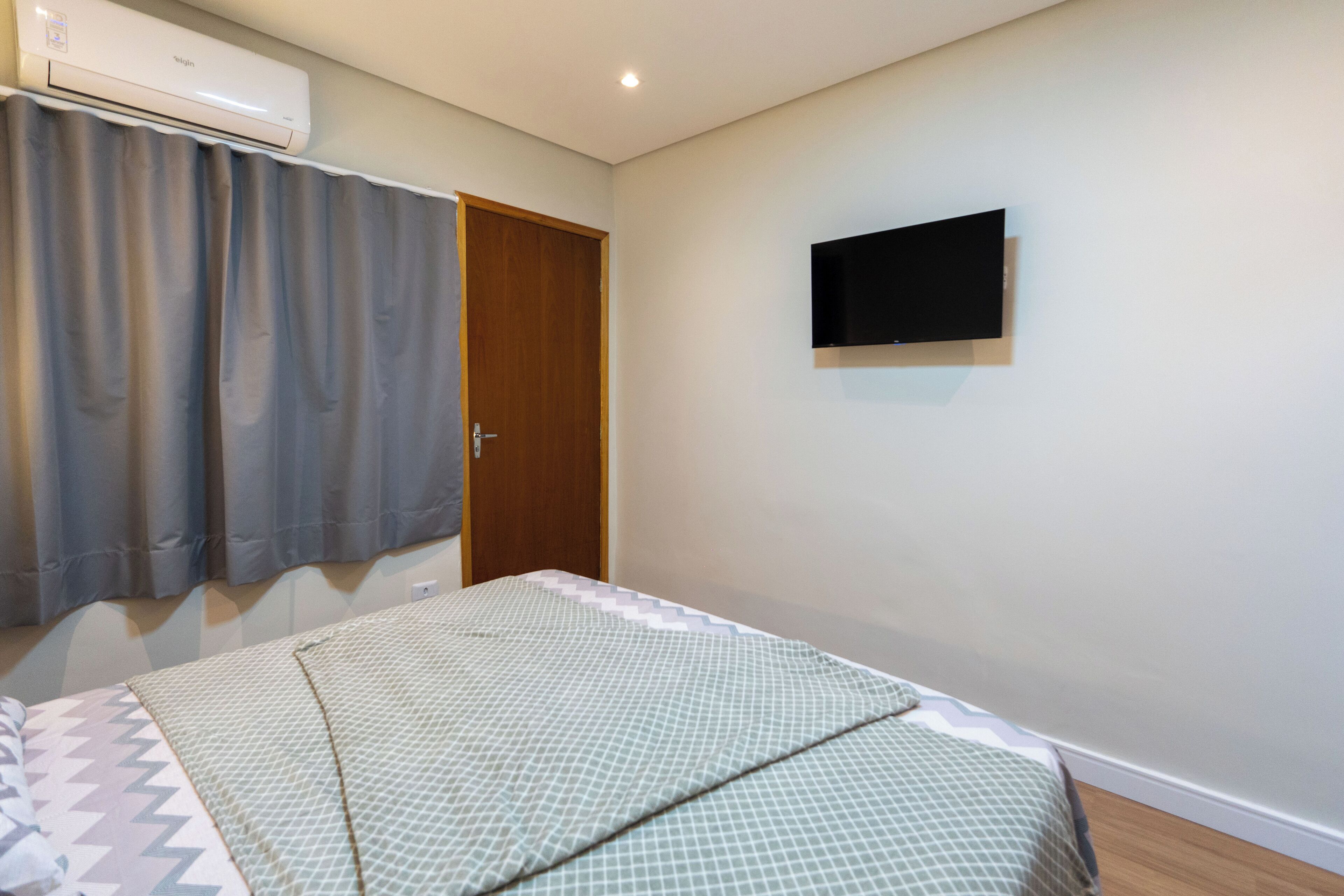 Ein Schlafzimmer mit einem Bett, einem an der Wand montierten Fernseher und einer Tür.