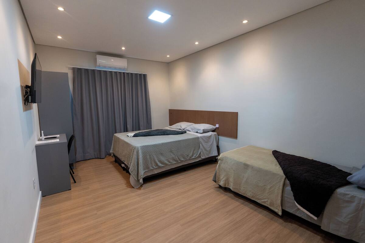 Quarto de hotel moderno com uma cama de casal, uma cama individual, uma escrivaninha e uma televisão.