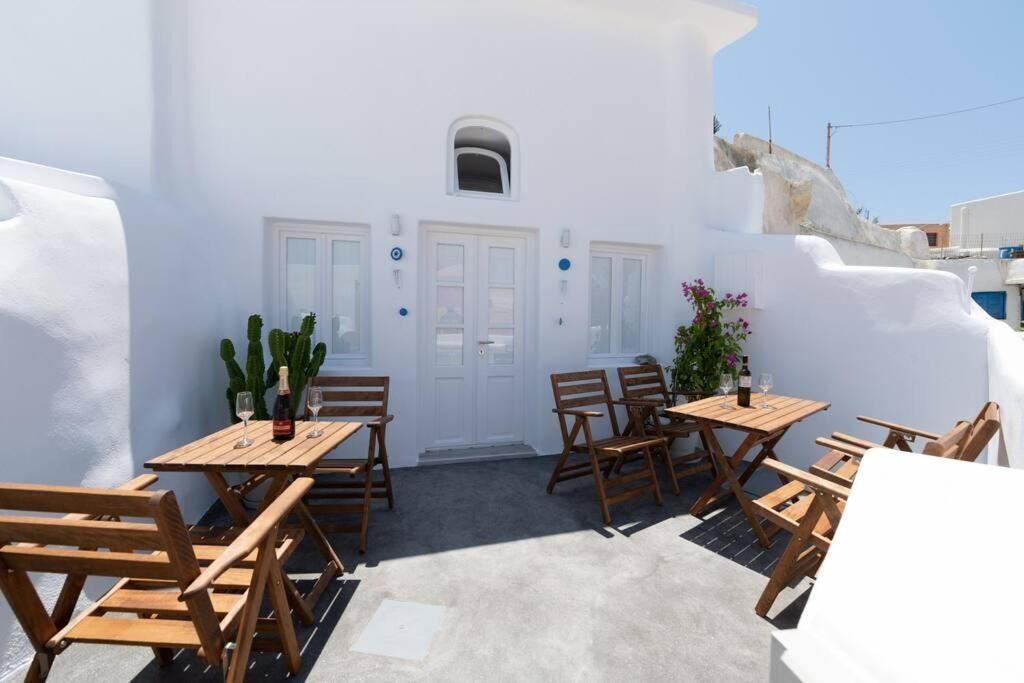 A white building with a door and windows, outdoor wooden furniture, and potted plants.