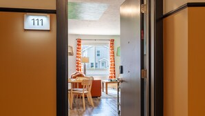A hotel room with a number 111 sign, a dining area with orange curtains, and a view of a building outside. - Le Nid Trailside 1BD Close to Beach/Downtown (Traverse City)