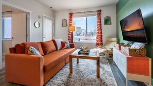 A living room with a sofa, coffee table, and a TV on a stand. - Le Nid Trailside 1BD Close to Beach/Downtown (Traverse City)