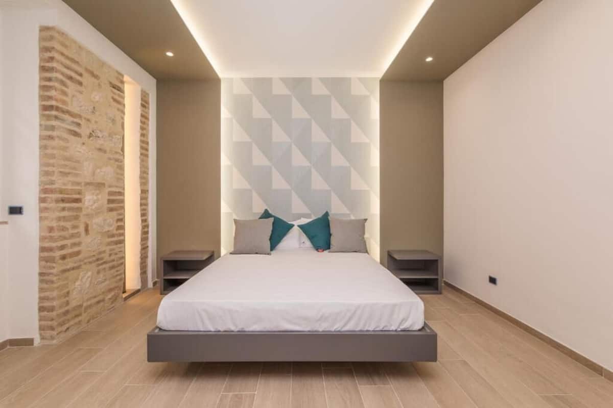 Un dormitorio moderno con cama, mesitas de noche y un muro con estampado geométrico.