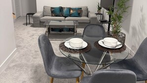 Una sala de estar moderna con un sofá gris, una mesa de centro de vidrio y una mesa de comedor preparada para dos.