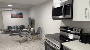 Una cocina moderna con horno y microondas integrados, un comedor con mesa y sillas de vidrio, y una sala de estar con sofá y un cuadro en la pared.