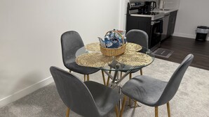 Una cocina moderna con microondas, cafetera y un lavamanos pequeño. Hay una mesa de comedor con cuatro sillas y una cesta de agua embotellada.