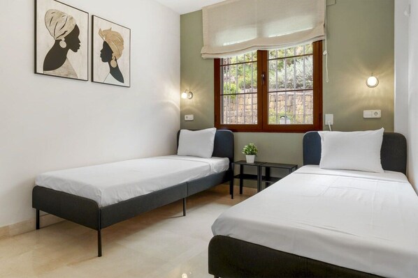 Una habitación con dos camas individuales, una mesita y una ventana con cortinas.