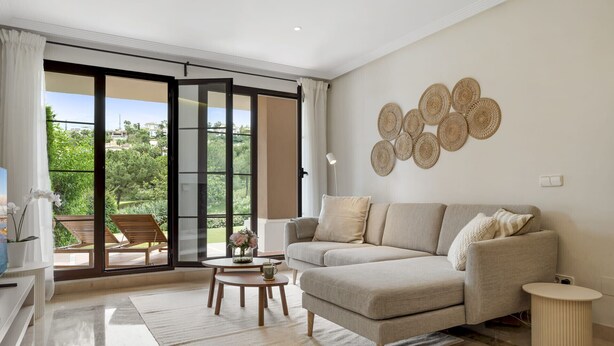 Un salon moderne avec un canapé, une table basse et une vue sur un jardin luxuriant, visible à travers de grandes portes-fenêtres coulissantes.