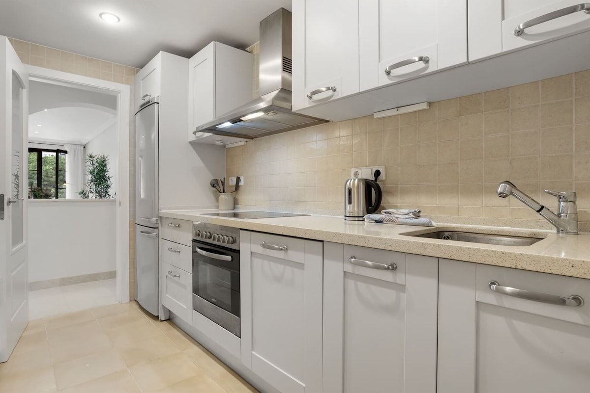 Una cocina moderna con gabinetes blancos, una campana de acero inoxidable, horno empotrado y un lavamanos con grifo.
