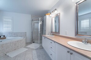 Une salle de bain moderne avec une baignoire, deux lavabos, une douche à l’italienne et de grands miroirs.