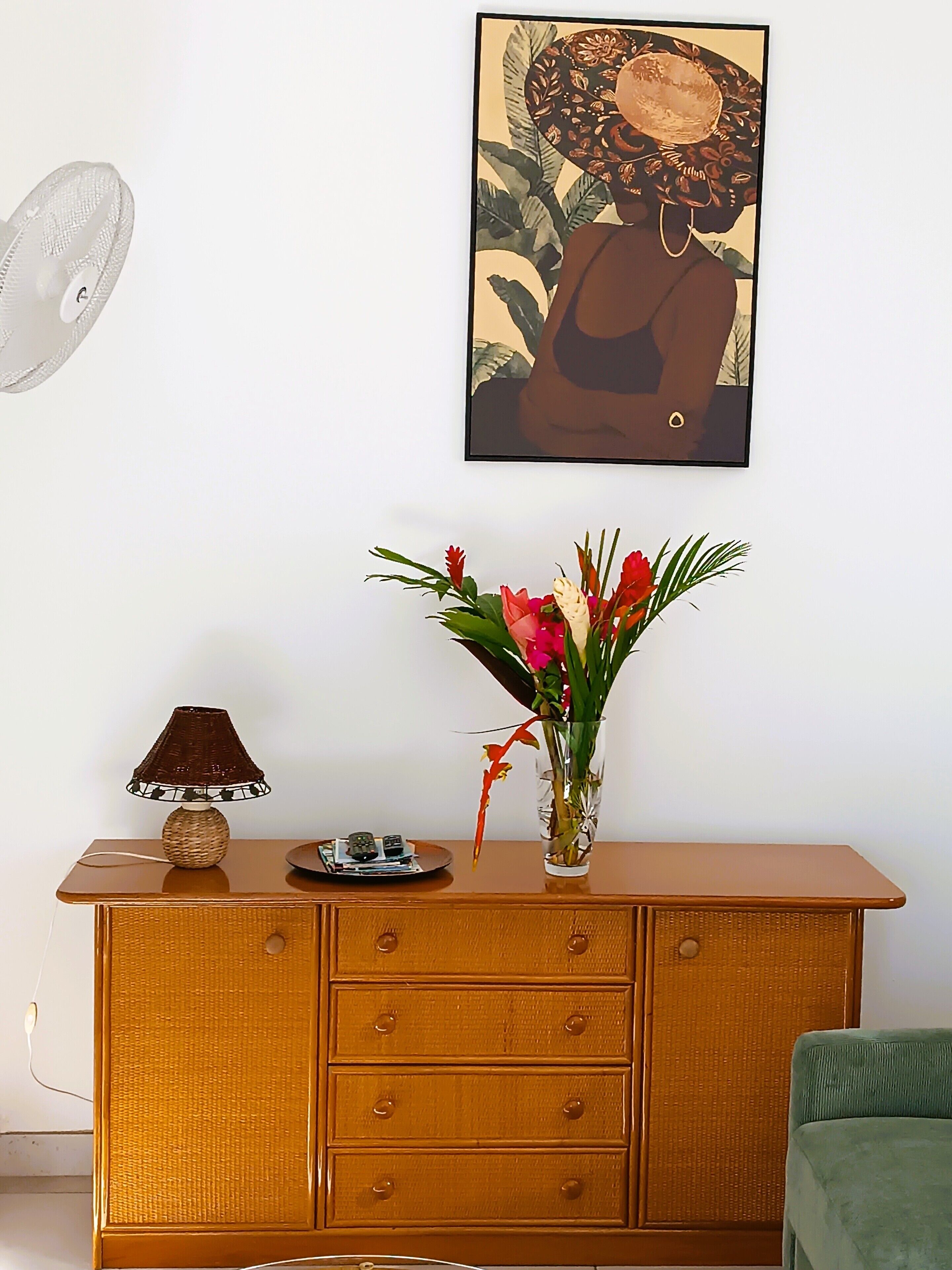 Une commode en bois avec des tiroirs, une lampe, une petite assiette avec des objets et un vase avec des fleurs.