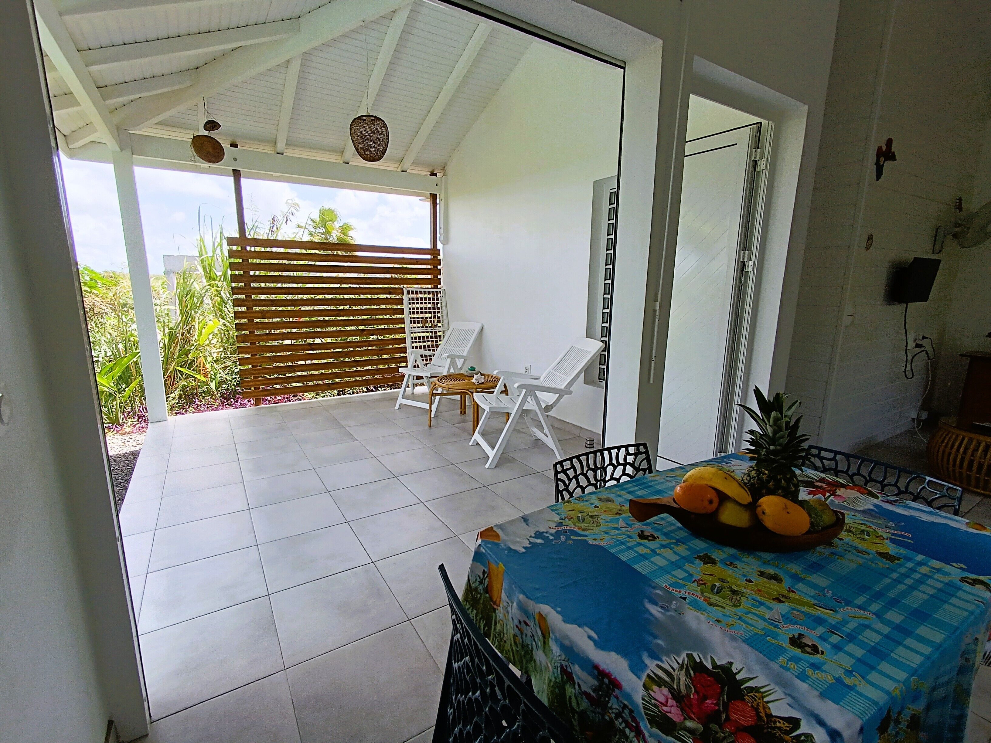 Une terrasse couverte avec une table dressée pour les repas, des chaises et une vue sur le jardin.