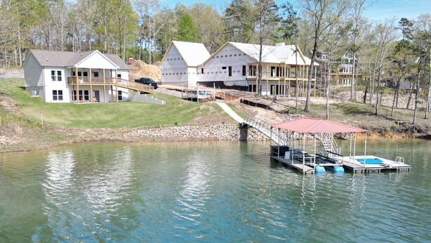 Une propriété au bord du lac comprenant plusieurs maisons reliées par un pont, un quai avec des bateaux et un mur de soutènement en pierre.