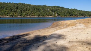 Une plage à l’eau claire, une rive sablonneuse et, en arrière-plan, une colline boisée.