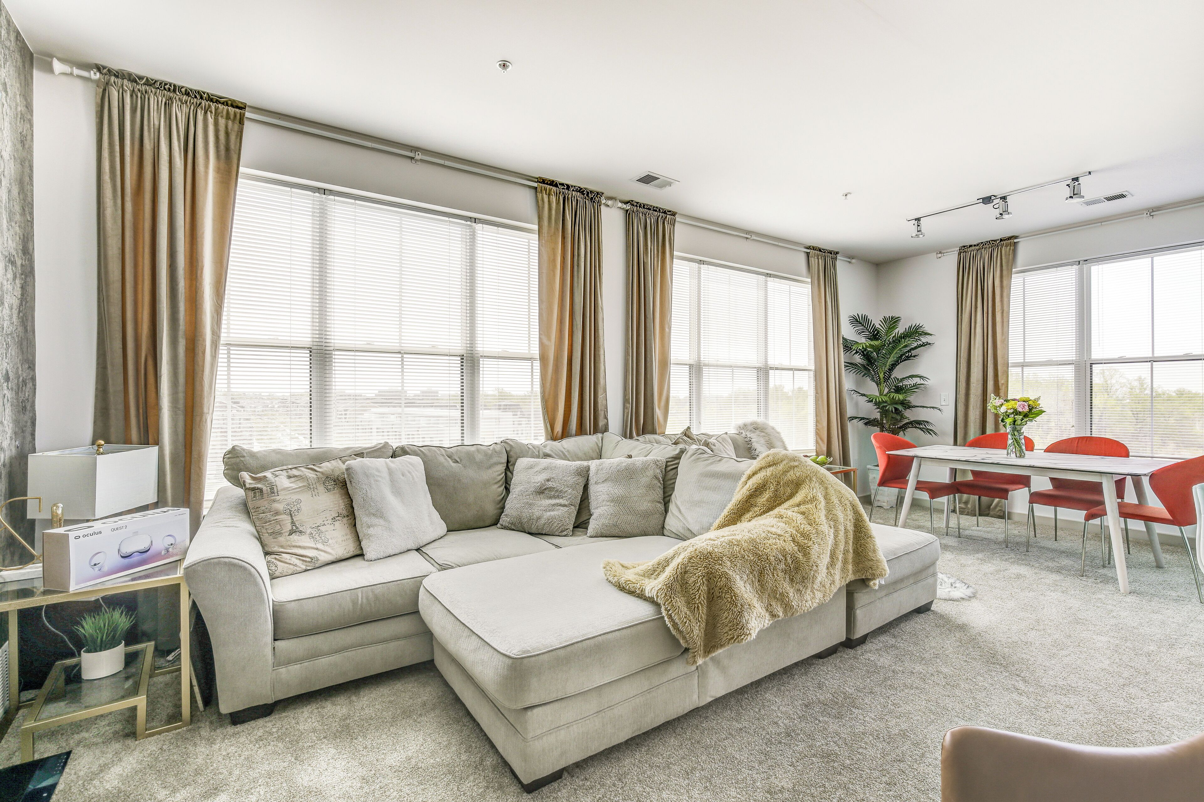 A modern living room with a sectional sofa, a dining table with chairs, and large windows with curtains.