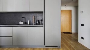 Une cuisine moderne avec des meubles gris, un plan de travail noir et une porte en bois à l’arrière-plan.