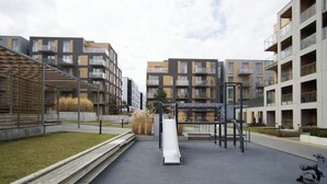 Un terrain de jeux équipé d’un toboggan et de structures d’escalade, entouré d’immeubles d’appartements modernes.