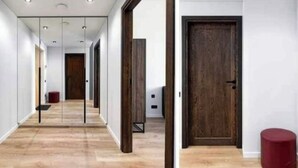 Un couloir avec un plancher en bois, une porte en bois et un tabouret rouge.