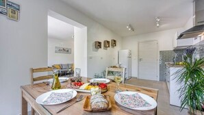 A dining area with a wooden table set for a meal, a kitchen in the background, and a potted plant on the right. - Family Apartment - Cosy & Modern, 850 meters to the Sea (Porec)