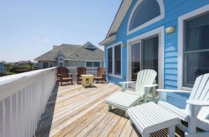 Relax on the deck with Adirondack chairs and a small table, surrounded by a white railing and a residential building with large windows.