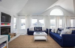 Relax in this spacious living room with a high ceiling, large windows, and a cozy fireplace.