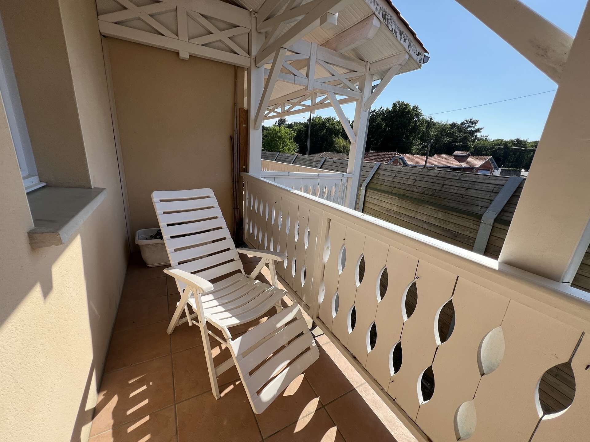 Un espace extérieur abrité, aménagé avec deux fauteuils blancs et une clôture en bois ornée d’ouvertures circulaires.