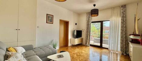 Una sala de estar moderna con un sofá, una mesa de centro, un televisor y un ventanal con cortinas.