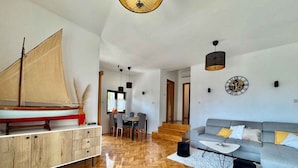 A spacious living area with a wooden herringbone floor, a grey sofa with yellow cushions, a wooden cabinet, and a sailboat model. - Holiday apartment with pool (Krk)