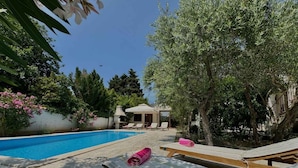 A pool area with lounge chairs and a pergola, surrounded by trees and a clear sky. - Holiday apartment with pool (Krk)