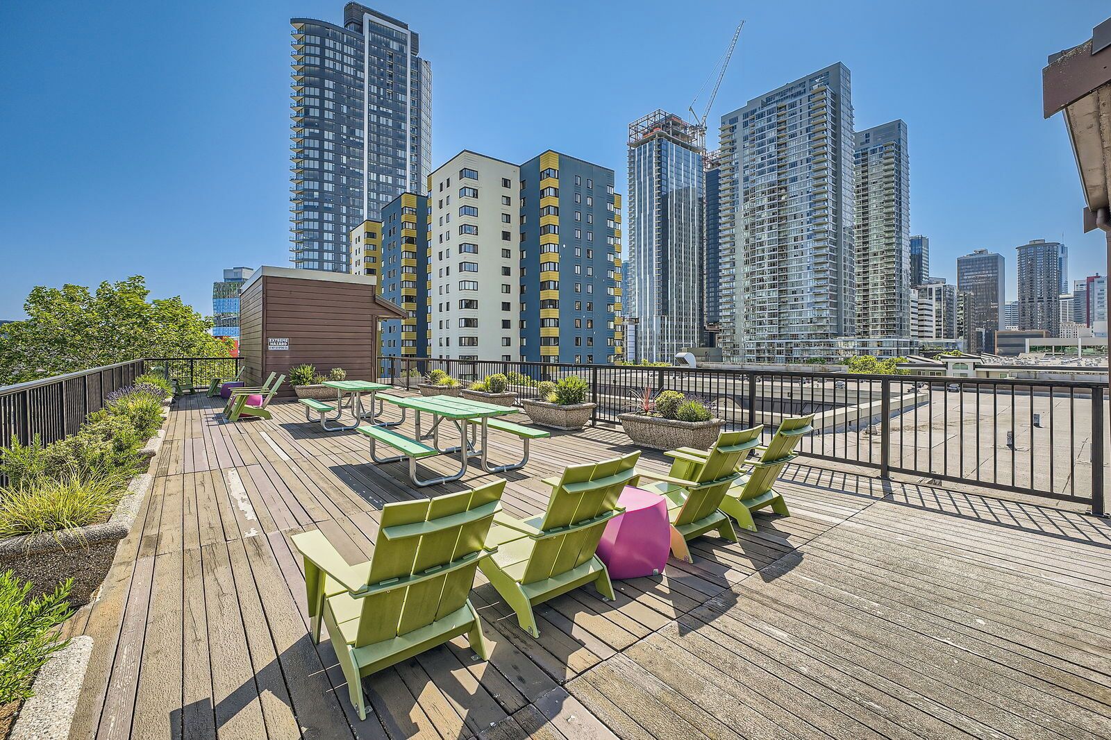A rooftop terrace with green chairs and tables, surrounded by a wooden deck and potted plants.