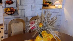 Ein Essbereich mit einer Steinwand, einer Vase mit getrockneten Blumen und Obstkörben auf Regalen.