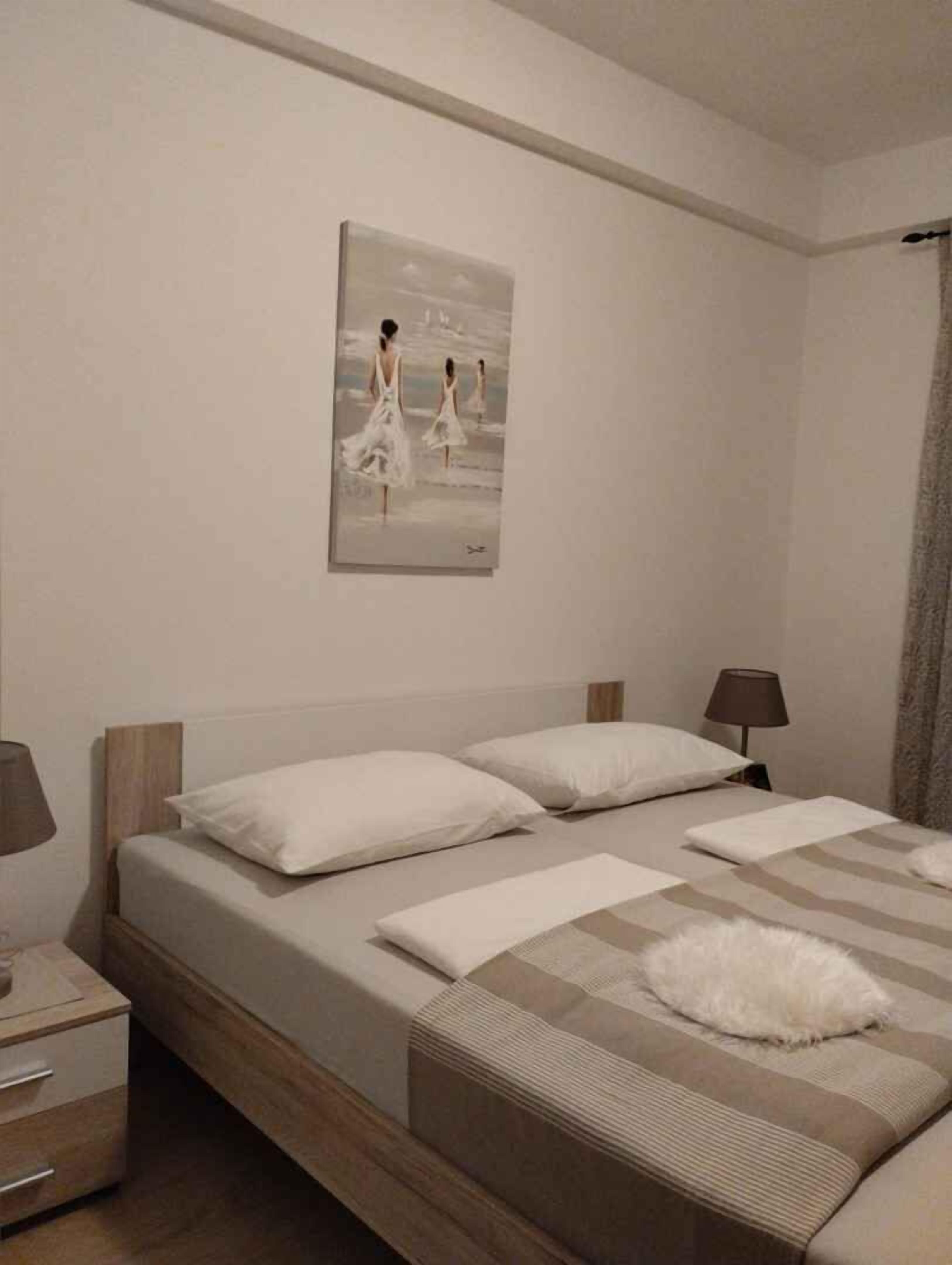 A bedroom with a bed, pillows, a bedside table, a lamp, and a painting on the wall.