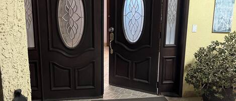 A double door with decorative glass panels, a potted plant, and a tiled entrance area.
