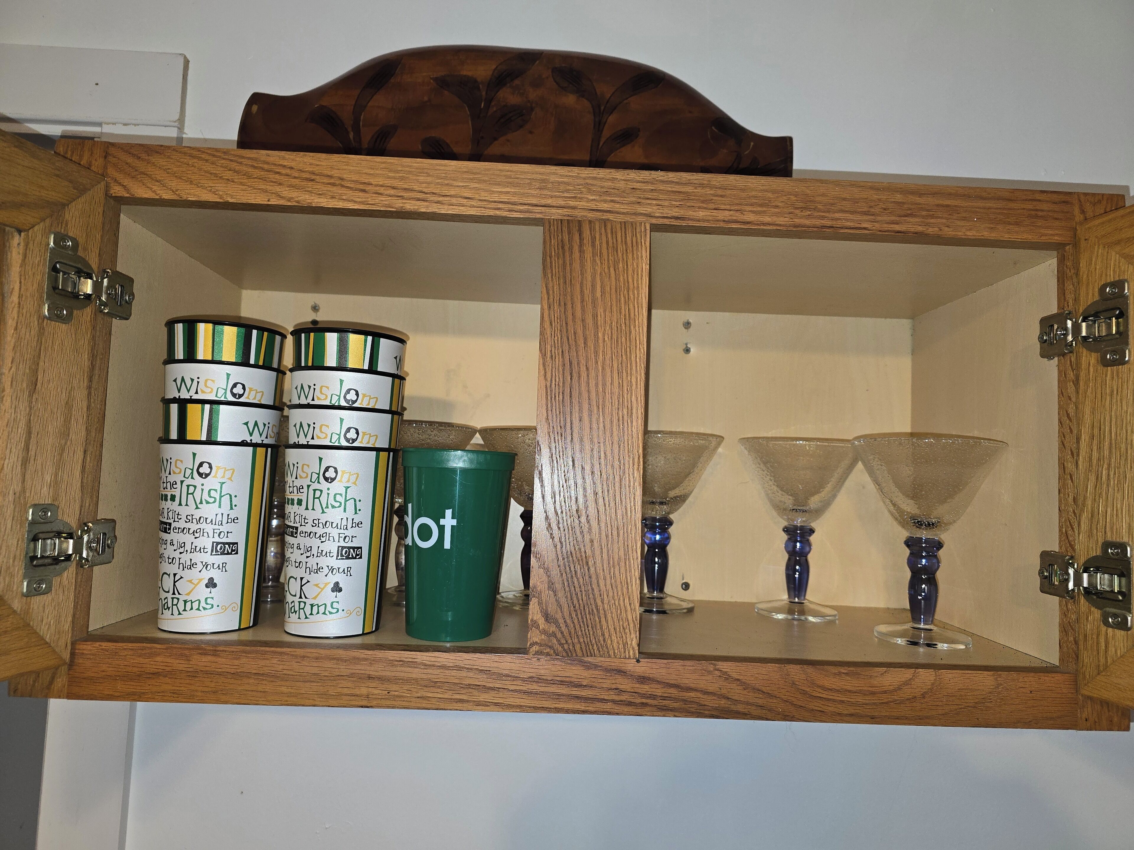 Un mobiletto in legno con tre barattoli etichettati 'Wisdom the Irish' e uno verde, e due bicchieri da martini in vetro.