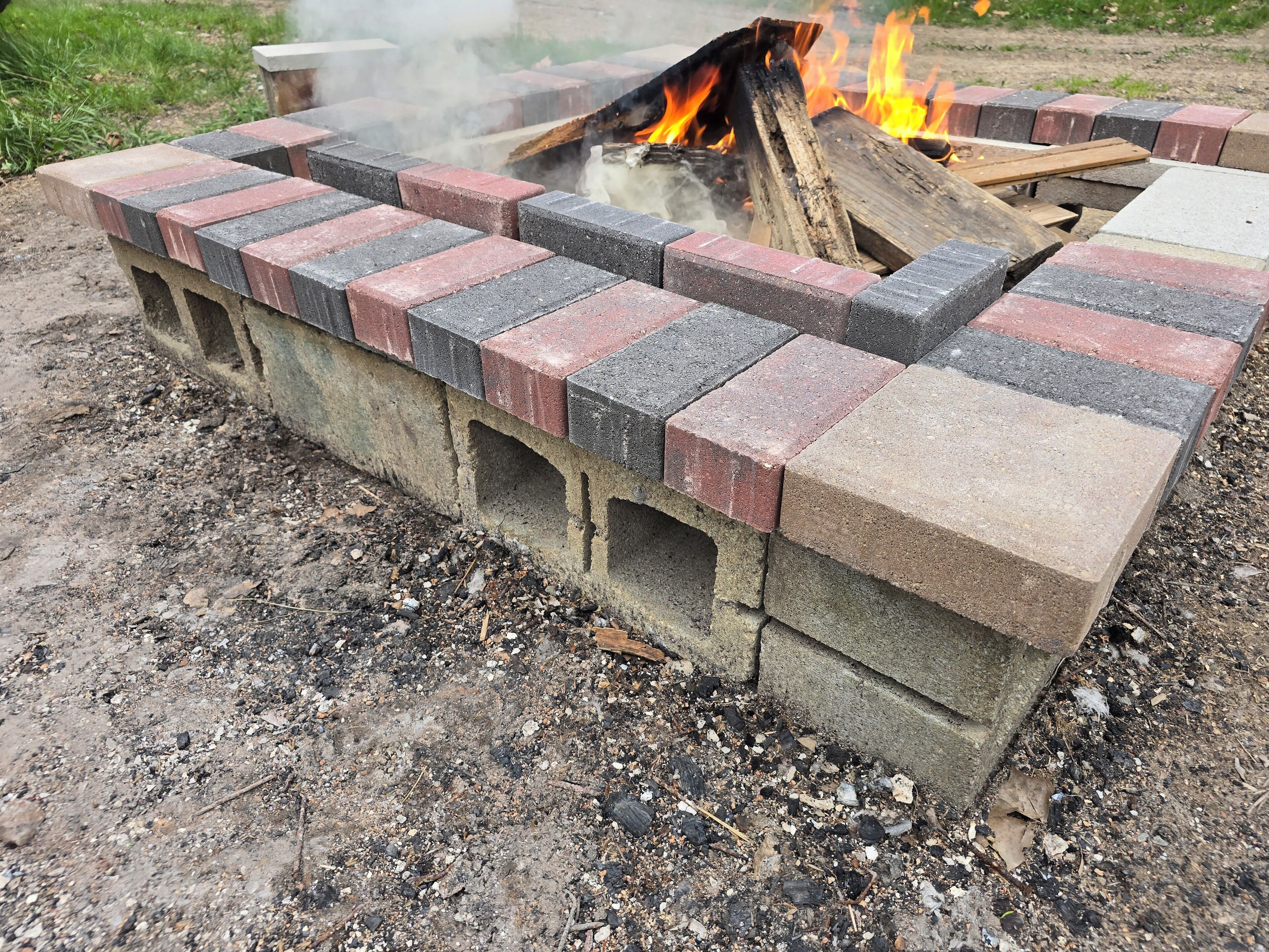 Ein Feuerkorb aus Beton mit einer Ziegelumrandung, umgeben von einer Kiesfläche.