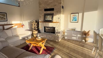 A modern living room with a stone fireplace, a wooden coffee table, and a large grey sofa.