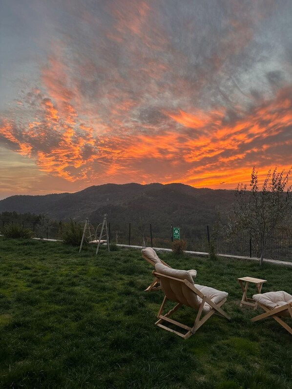 A sunset view with a grassy area, two wooden lounge chairs, and a small table. - Bona Dea Butik Otel  (Ayvacik)