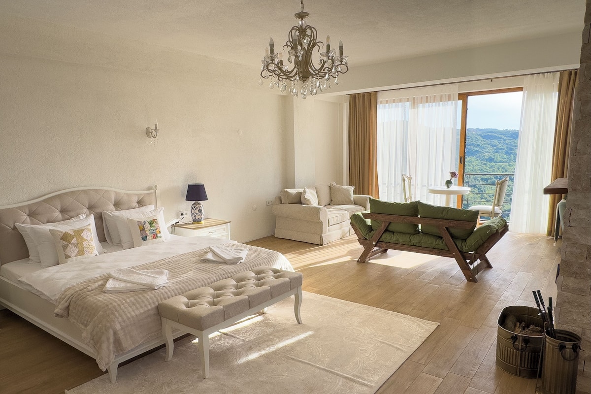 Een ruime slaapkamer met een groot bed, een zithoek met een groene bank en een balkon met uitzicht.