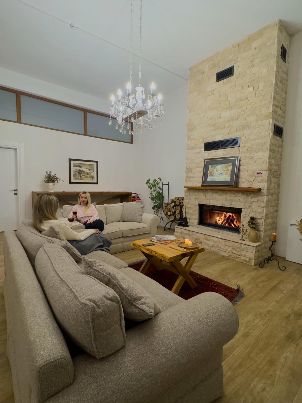 A living room with a stone fireplace, a chandelier, and a sofa.